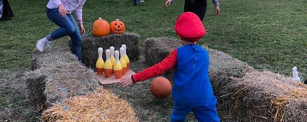 child in costume bowling with a pumpkin