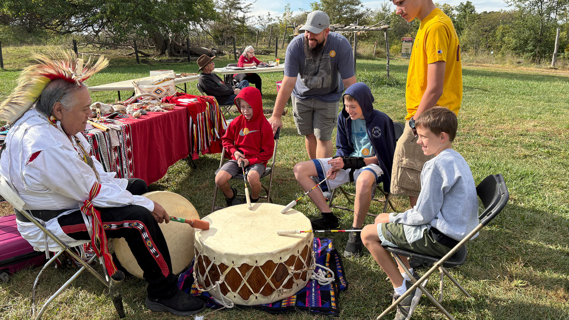 children drumming with man wearing traditional Indigenous clothing