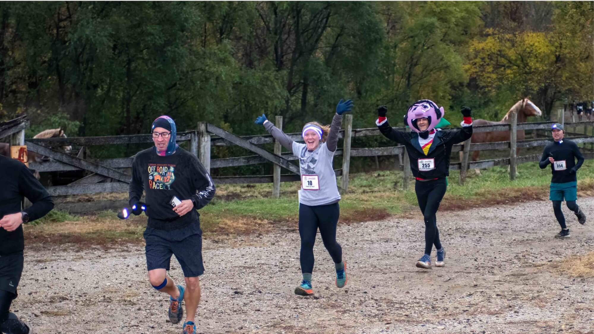 runners including man in count costume passing horse corral